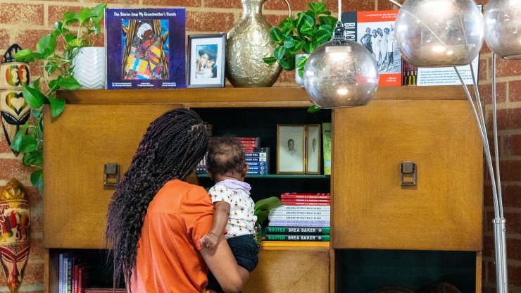 A woman holding a baby examines objects in the living room created for the Black Future Newsstand exhibit in Los Angeles