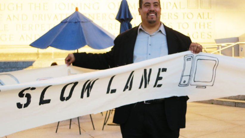 Man stands in front of banner symbolizing an internet "slow lane"