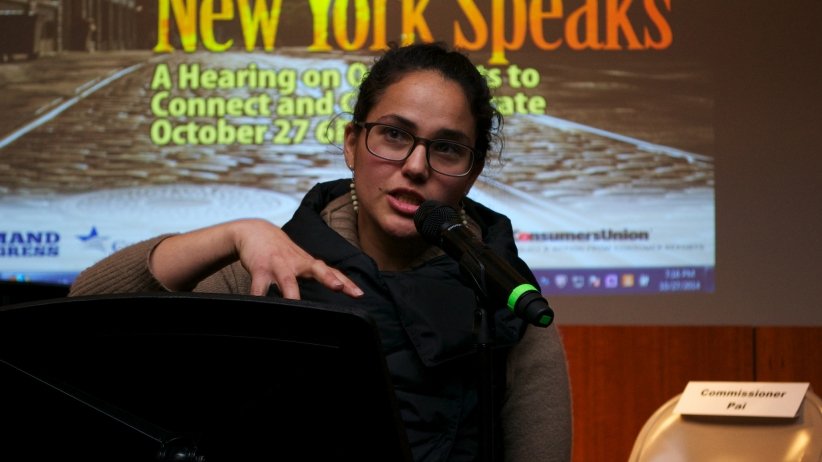 Woman speaks into microphone in front of screen reading "New York Speaks"