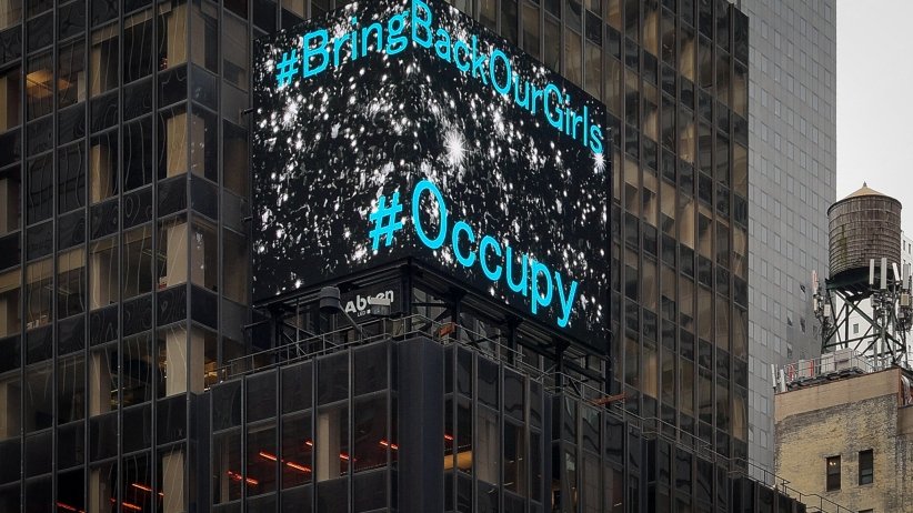 Video billboard reading "#BringBackOurGirls" and "#Occupy"