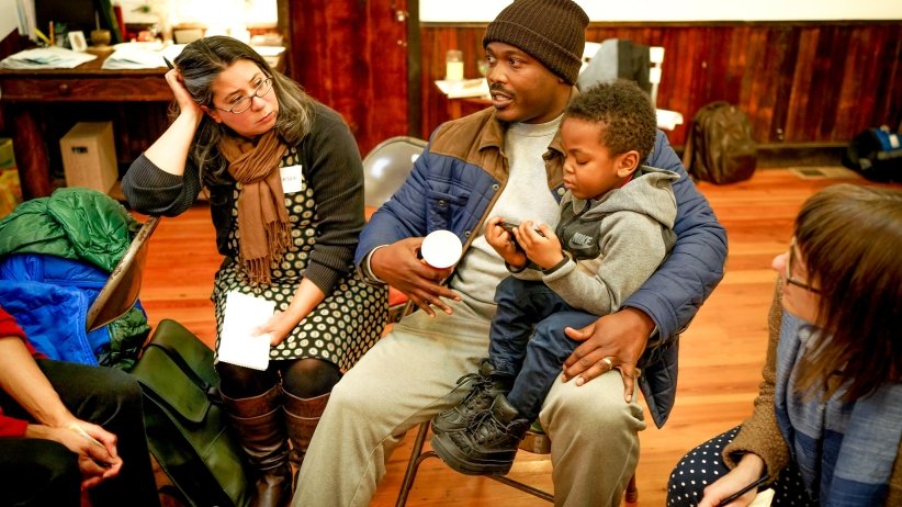 Man cradling a toddler in his lap while talking to others