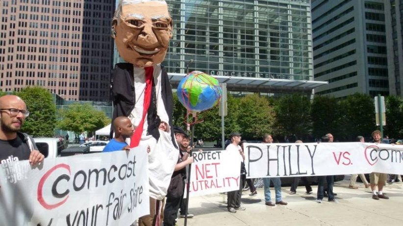 Activist on stilts portraying Comcast CEO Brian Roberts, surrounded by activists holding banners