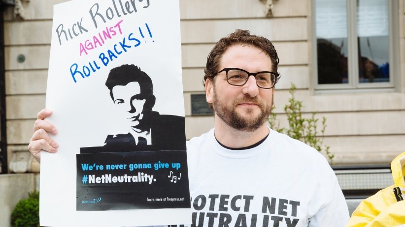 Net Neutrality activist holding sign reading "Rick Rollers Against Rollbacks"