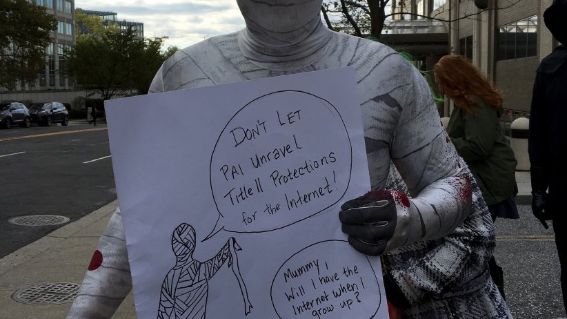 Man dressed up as a mummy with a sign reading "Don't let Pai unravel Title II protections for the internet"