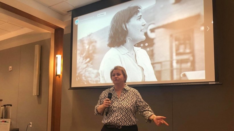 Woman speaking in microphone in front of a slide of a smiling woman