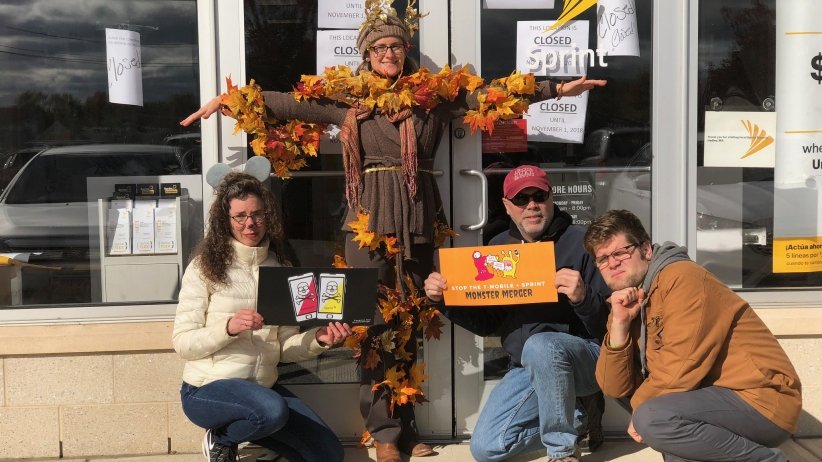 A woman dressed as a mouse, a woman dressed as a tree and two men pose with anti-merger signs