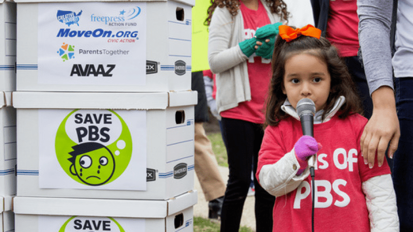 Young girl speaking into microphone beside petition boxes