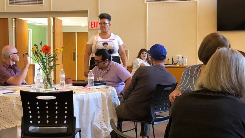 News Voices' Alicia Bell standing in front of people seated at various tables