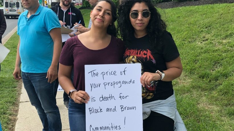 Activists holding banner reading "The price of your propaganda is death for Black and Brown communities"