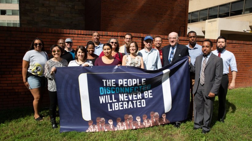 Group of people holding banner reading "The People Disconnected Will Never Be Liberated"