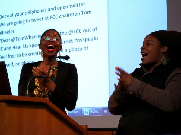 Two women at microphone in front of screen with text to Chairman Wheeler
