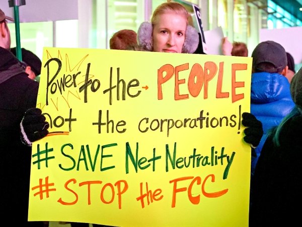 Net Neutrality activist holding sign reading "Power to the people, not corporations / Save Net Neutrality / #StoptheFCC"