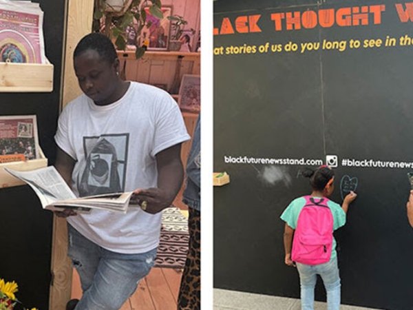Two visitors at the Media 2070 "Black Future Newsstand" exhibit: a man on the left reading a newspaper and a child on the right writing on the Black Thought Wall