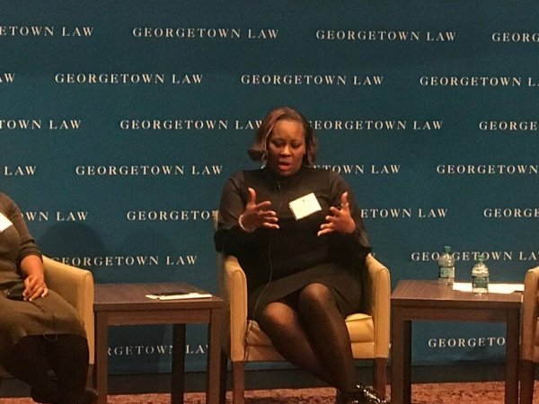 Three people engaged in a discussion on stage at the Color of Surveillance conference.