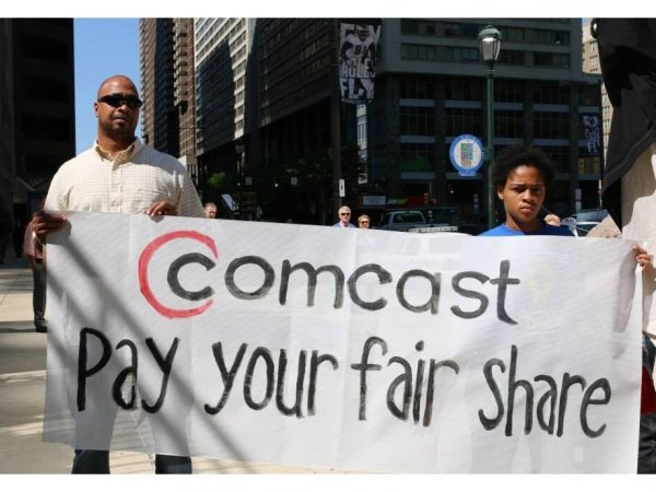 A father and son at a Philly protest holding a banner reading "Comcast: Pay your fair share"