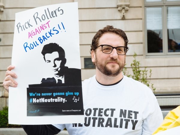 Net Neutrality activist holding sign reading "Rick Rollers Against Rollbacks"
