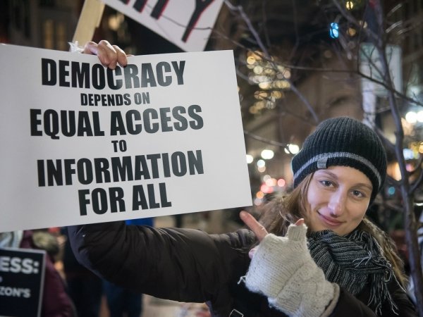 Woman holding sign reading "Democracy depends on equal access to information for all"