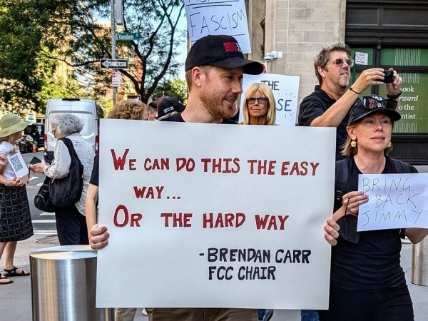 A protester holding a sign reading "We can do this the easy way or the hard way," Brendan Carr, FCC chair
