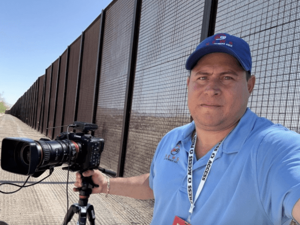 Journalist Mario Guevara holding a camera next to a fence
