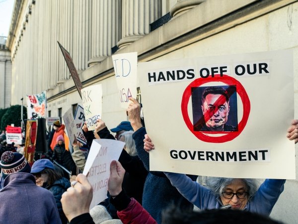 Protesters outside the U.S. Treasury Department holding a poster with an image of Elon Musk and the caption "Hands Off Our Government"