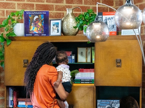 A woman holding a baby examines objects in the living room created for the Black Future Newsstand exhibit in Los Angeles
