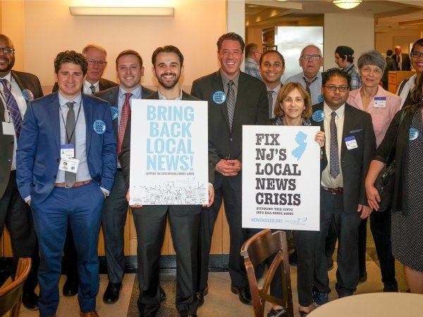 Group of people holding signs reading "Bring back local news" and "Fix NJ's local news crisis"