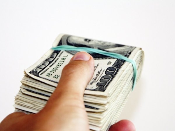A hand holding a wad of $100 bills