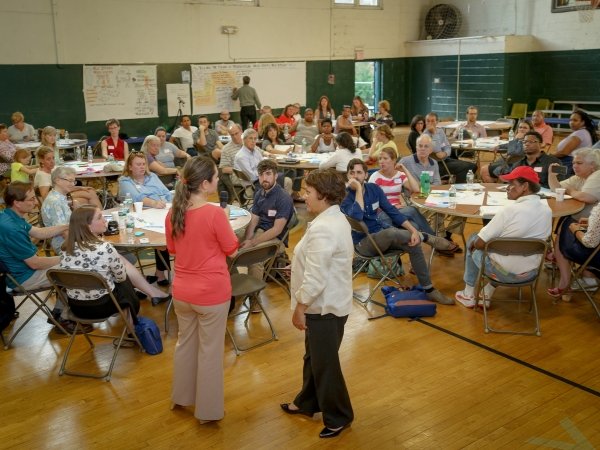 Two people standing and other people sitting at tables in the background