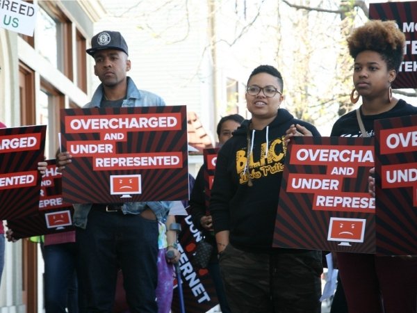 Activists holding posters reading "Overcharged and underrepresented"