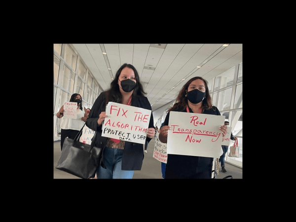 Rose Lang-Maso and another activist holding signs reading "Fix the algorithm" and "Real transparency now"