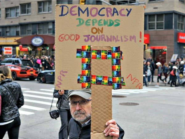 Man holding sign saying "Democracy depends on good journalism"
