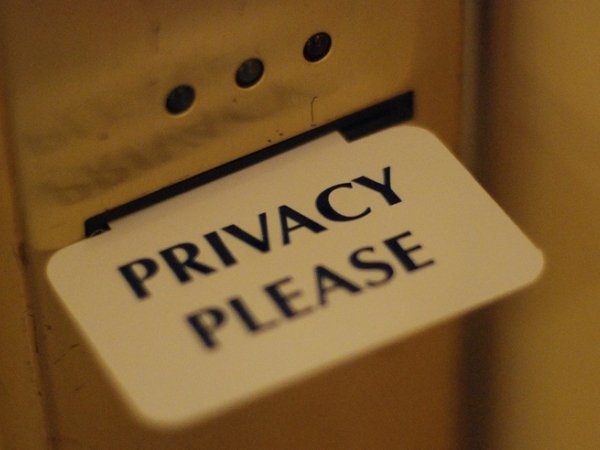 Card reading "Privacy please" sticking out from the slot of a hotel-room door.
