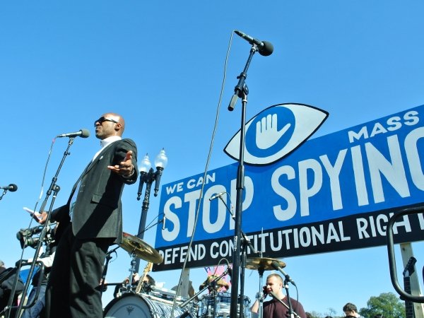 Man speaking at a protest before a banner reading "We can stop mass spying / defend constitutional rights"