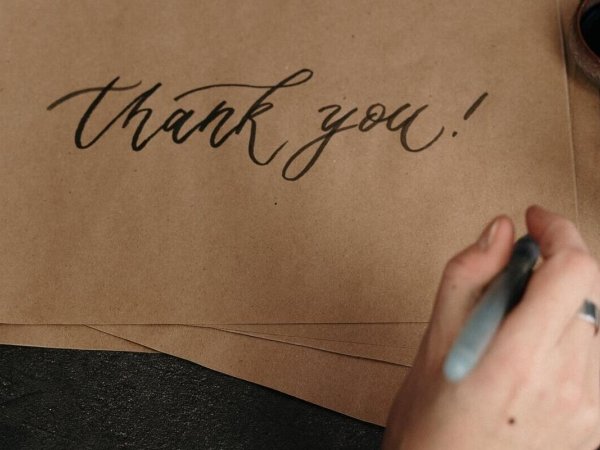 Person writing "thank you!" on a piece of brown paper