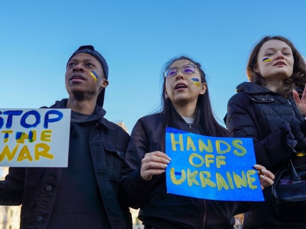 Three protesters holding signs reading "Stop the war" and "Hands off Ukraine"