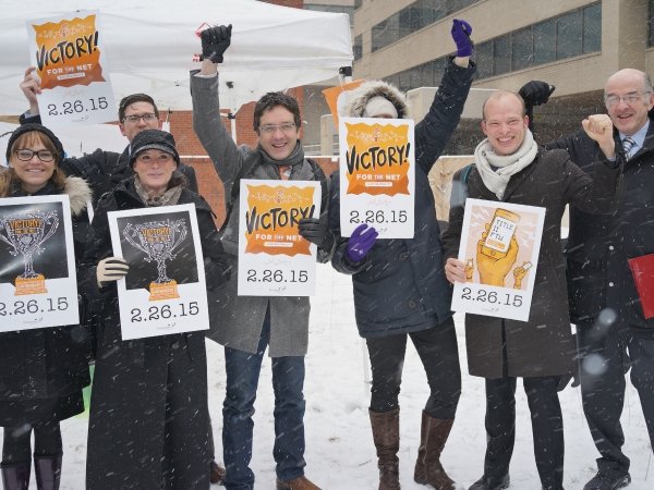 Activists standing in the snow holding "Victory: 2-26-15" signs