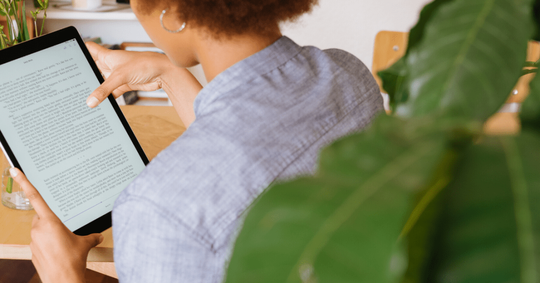 Person reading from mobile tablet at home next to green potted plant