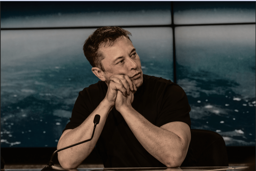 Elon Musk sitting at a microphone