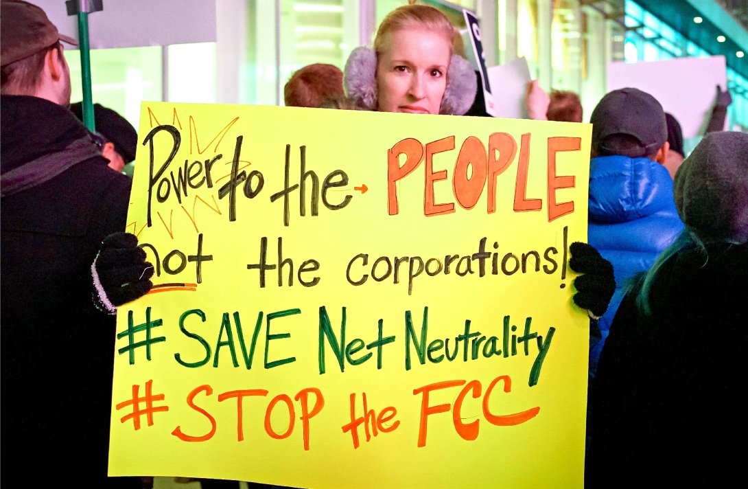 Net Neutrality activist holding sign reading "Power to the people, not corporations / Save Net Neutrality / #StoptheFCC"