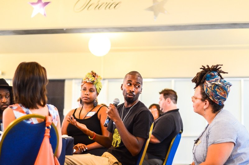 A man at a table with other people speaks into a microphone