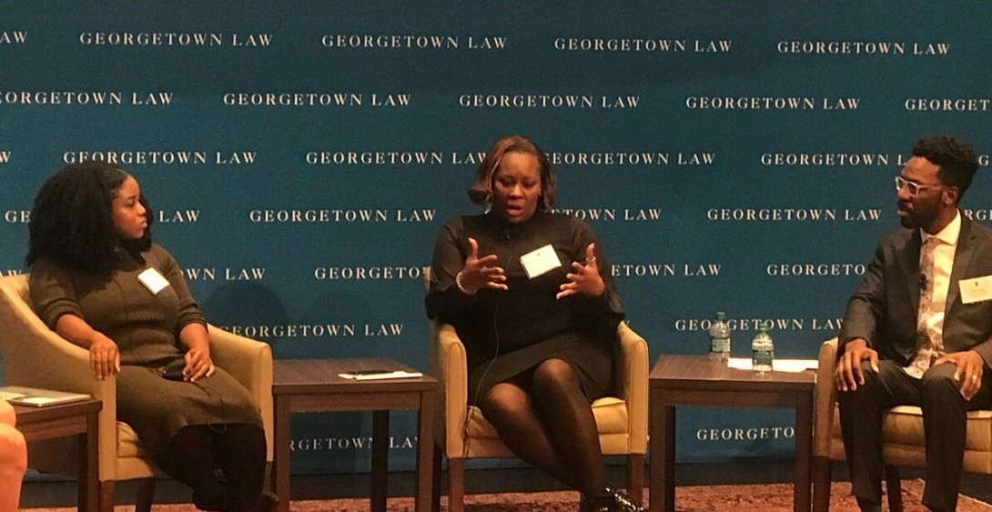 Three people engaged in a discussion on stage at the Color of Surveillance conference.