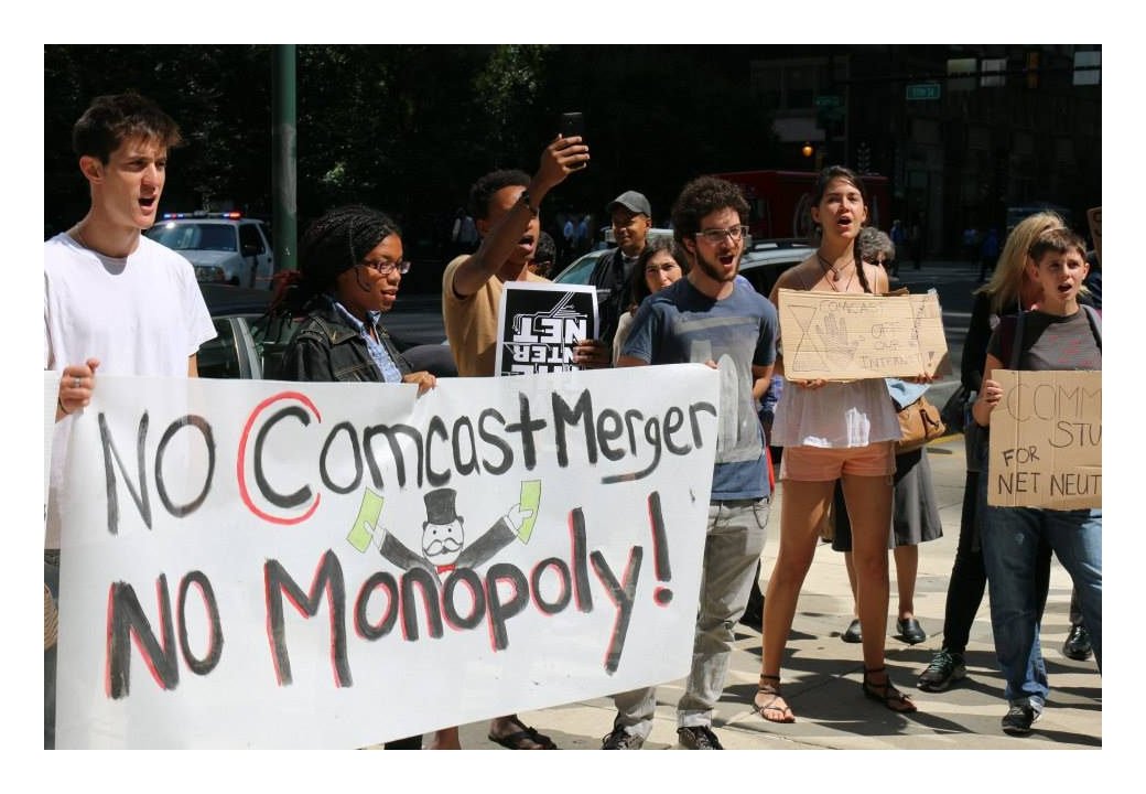 Activists holding banner reading "No Comcast merger / no monopoly"
