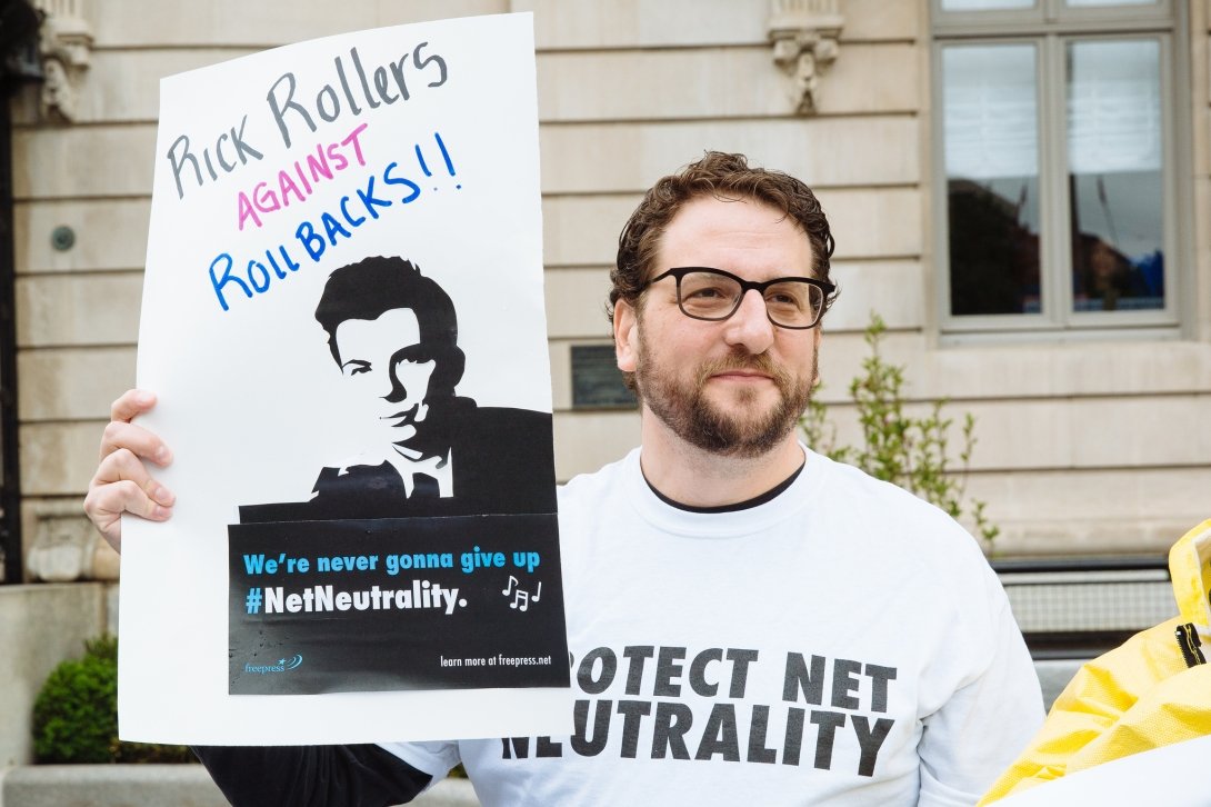 Net Neutrality activist holding sign reading "Rick Rollers Against Rollbacks"