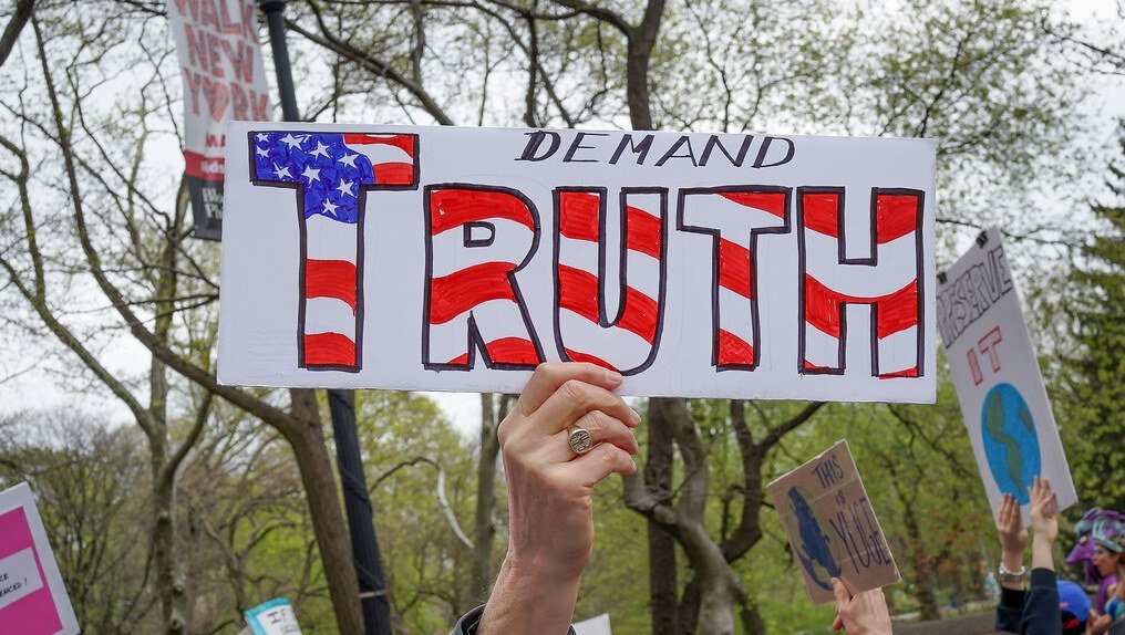 Protester holding a sign reading "Demand truth"