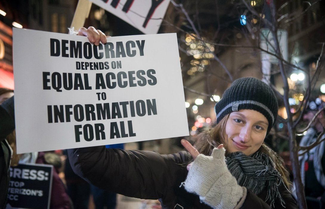 Woman holding sign reading "Democracy depends on equal access to information for all"