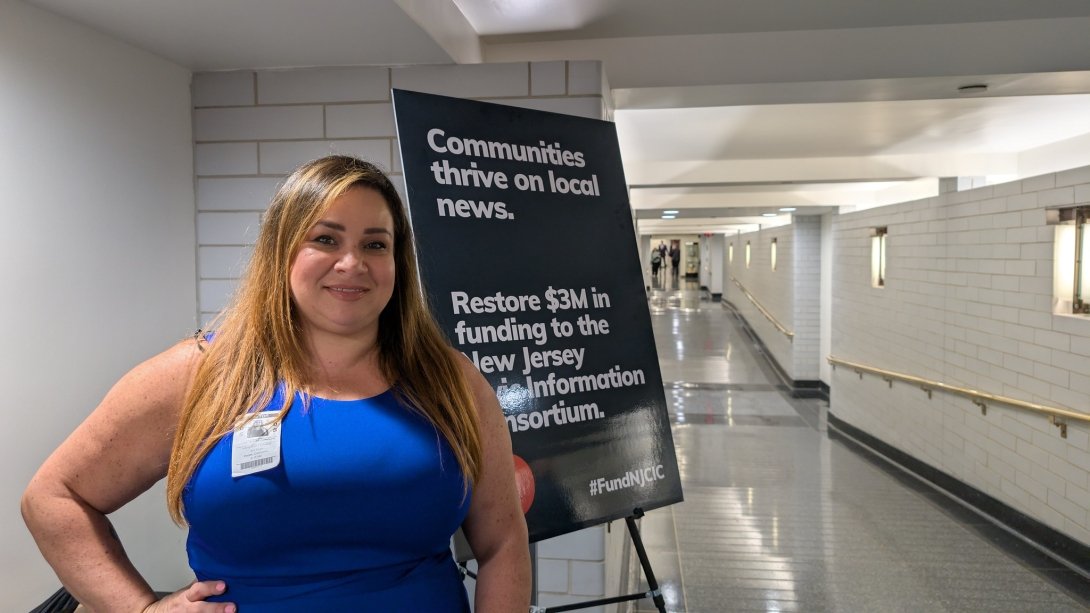 Free Press Action's Vanessa Maria Graber standing beside a sign at the New Jersey statehouse