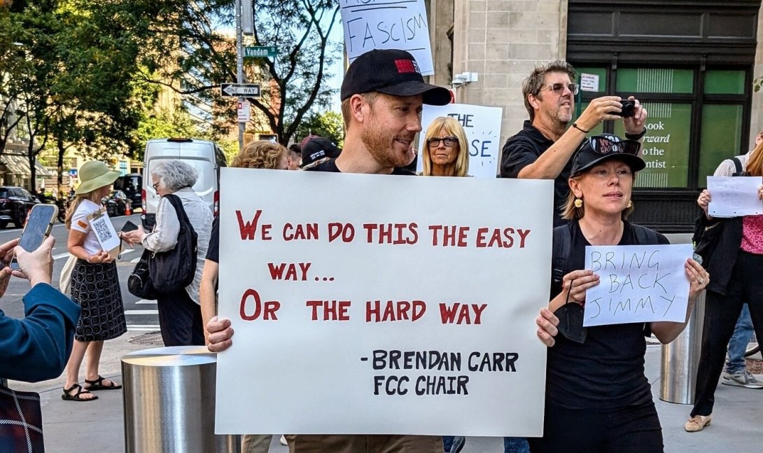A protester holding a sign reading "We can do this the easy way or the hard way," Brendan Carr, FCC chair