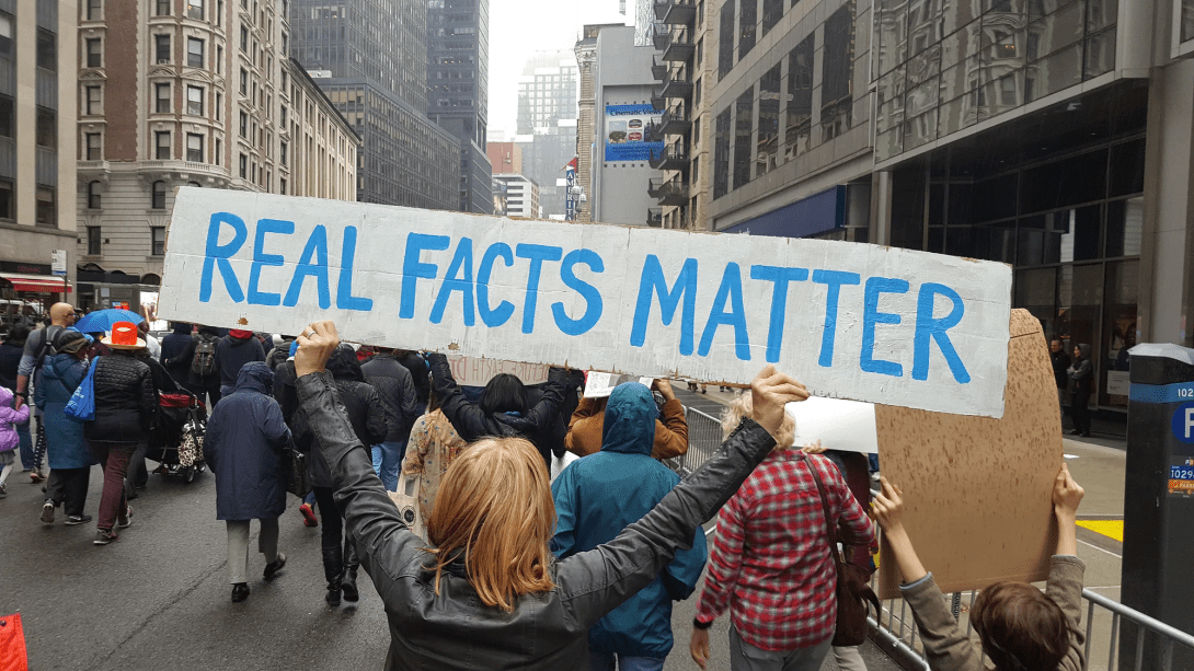 A protester holding a sign reading "Real Facts Matter"