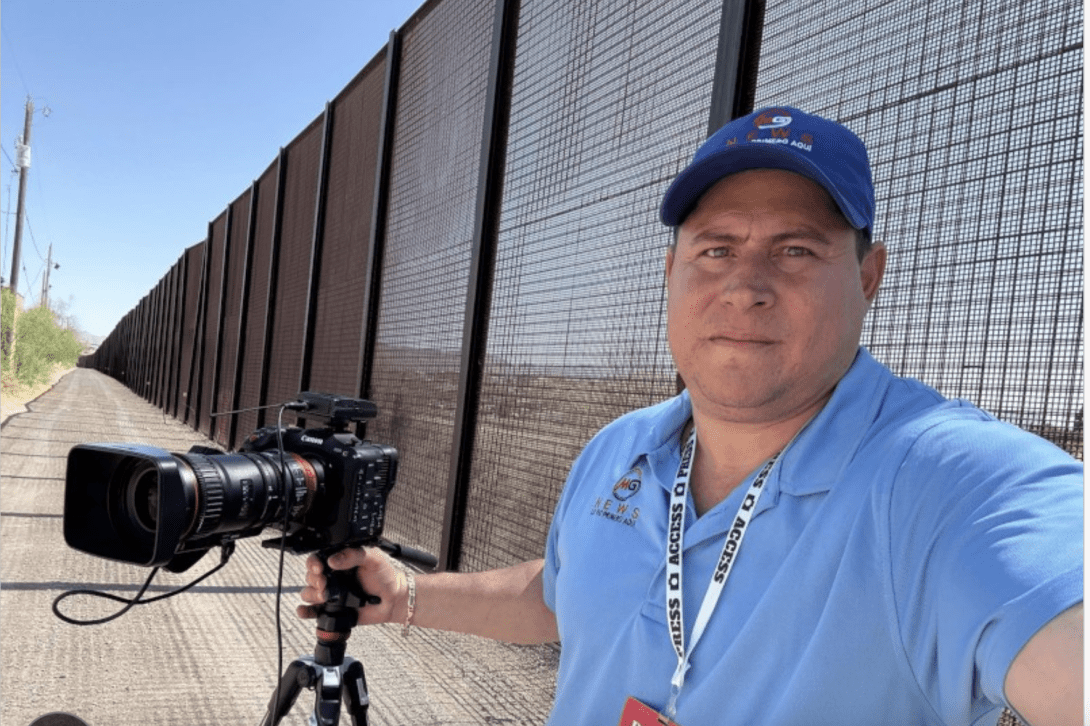 Journalist Mario Guevara holding a camera next to a fence
