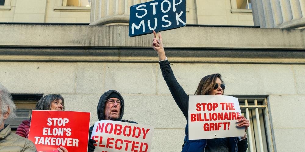 Protesters holding signs reading "Nobody elected Musk" and "Stop the billionaire grift"